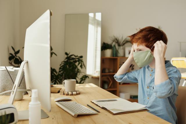 Boy wearing a mask while doing school from home on a computer