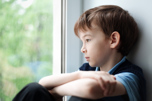 Sad boy, sitting alone, gazing out a window